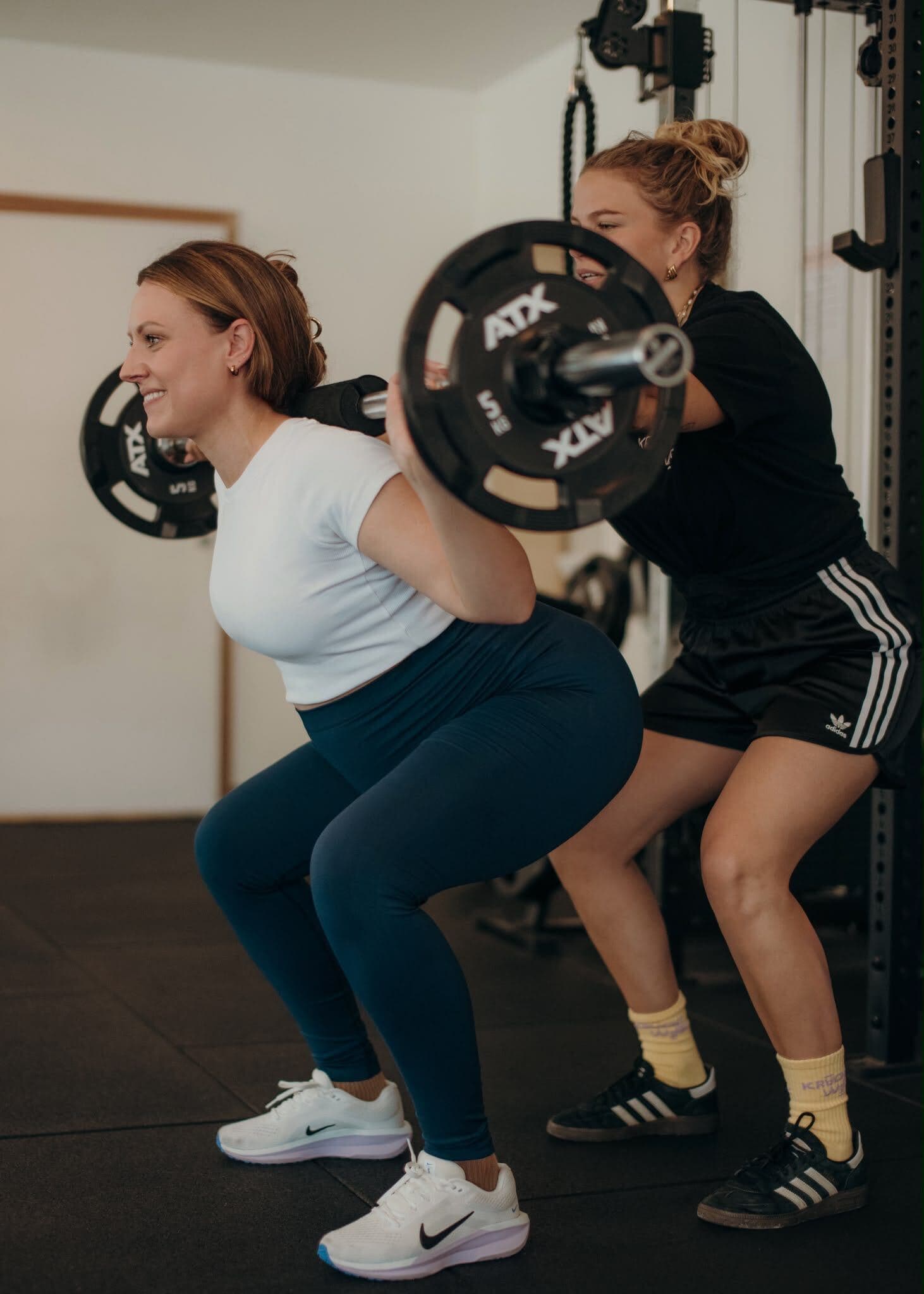 Coach begeleidt een squat met de barbell bij Krachtwerk